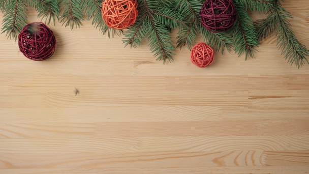 Πρωτοχρονιά και Χριστουγεννιάτικη διακόσμηση. Χέρι βάζει κάποια δώρα, ξύλινα χρωματιστές μπάλες κοντά στα κλαδιά χριστουγεννιάτικο δέντρο σε ένα ξύλινο τραπέζι. Ασημένια αστέρια πέφτουν στο τραπέζι. Η διακόσμηση του χριστουγεννιάτικου δέντρου είναι στον τελικό δρόμο. Άνω όψη - Πλάνα, βίντεο