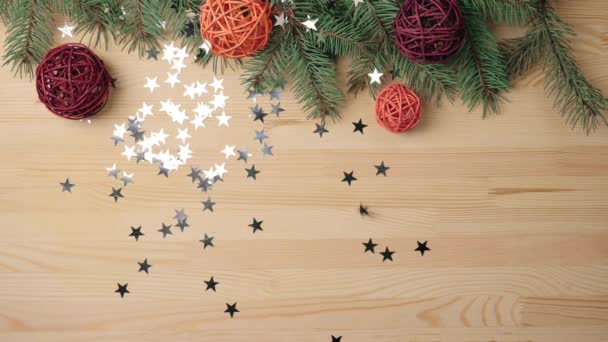 Újévi és karácsonyi dekoráció. Kézzel tesz néhány ajándékot, fa színű golyókat közel a karácsonyfa ágak egy fa asztalra. Ezüst csillagok hullanak az asztalra. A karácsonyfa díszítése a végső úton van. Felülnézet - Felvétel, videó