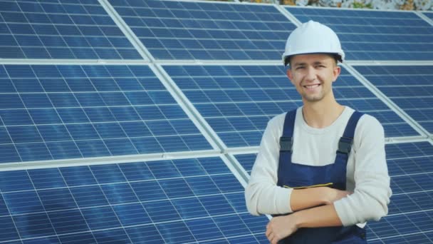 Portrait of a young worker in a white helmet on the background of solar panels - Filmati, video