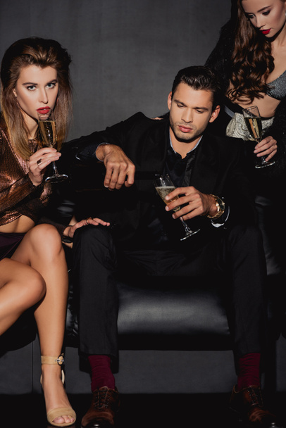 handsome man  pouring champagne for attractive and stylish women isolated on black - Photo, Image