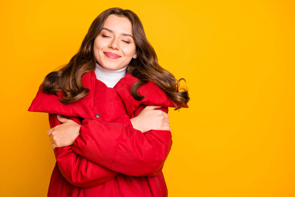 Photo of charming lady traveler enjoy warm weather hugging shoulders eyes closed overjoyed wear red warm winter outerwear coat isolated yellow color background - 写真・画像