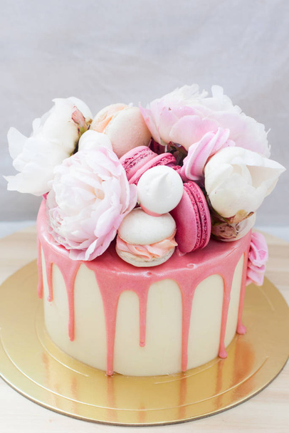 White cake with pink melted chocolate, fresh roses and peonies, macaroons and meringues.  - Valokuva, kuva