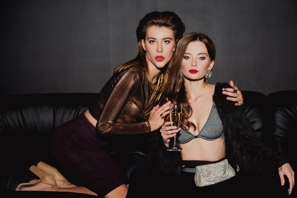 attractive and stylish woman hugging friend with champagne glass isolated on black - Φωτογραφία, εικόνα