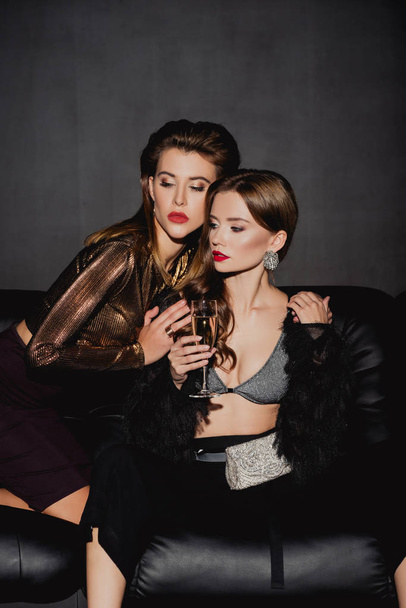 attraktive und stilvolle Frau umarmt Freund mit Champagnerglas isoliert auf schwarz - Foto, Bild