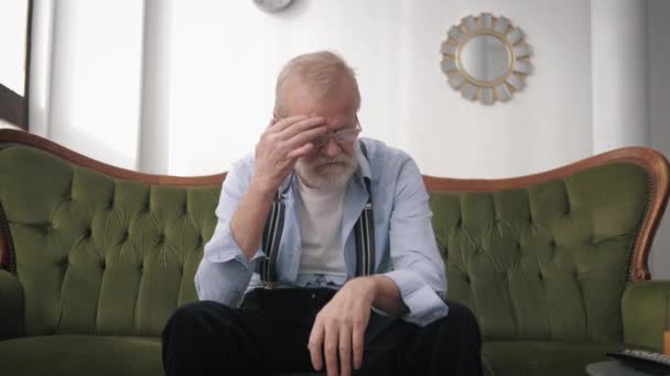 špatné zdraví, starý muž trpící bolestí hlavy migréna rozrušený životem sedí na pohovce v pokoji, koncept osamělosti - Záběry, video