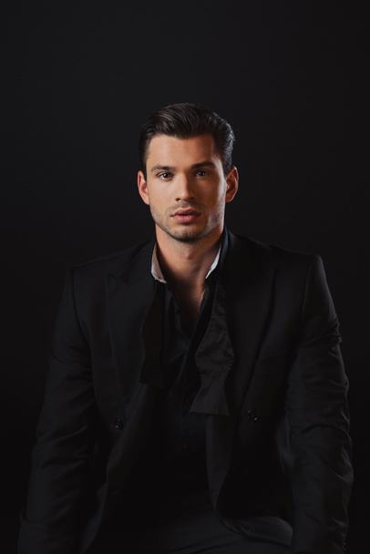 handsome man in suit looking at camera isolated on black - Photo, Image