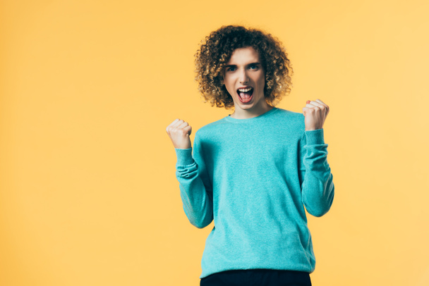 excited curly teenager screaming and showing yeah gesture isolated on yellow - Foto, immagini