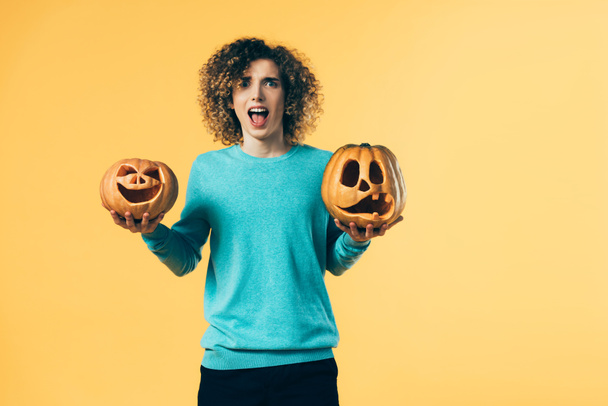 scared curly teenager holding Halloween pumpkins and screaming isolated on yellow - Foto, immagini
