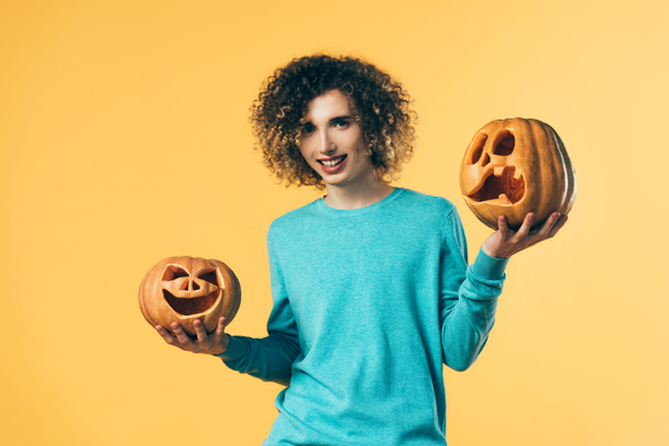sonriente rizado adolescente celebración de Halloween calabazas aislado en amarillo
 - Foto, imagen