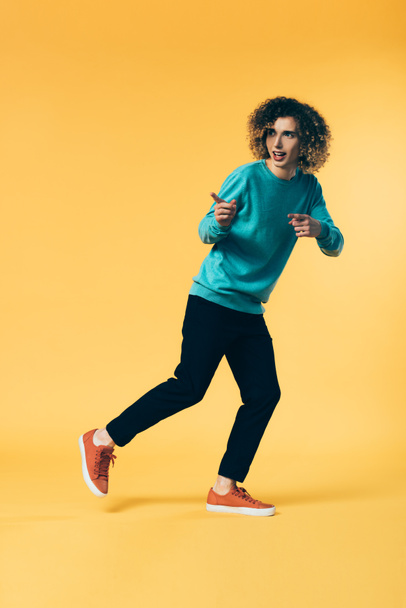 full length view of curly teenager running and pointing with fingers on yellow - Fotografie, Obrázek