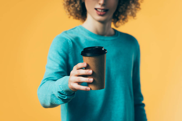 selective focus of curly teenager holding coffee in paper cup isolated on yellow - Fotografie, Obrázek