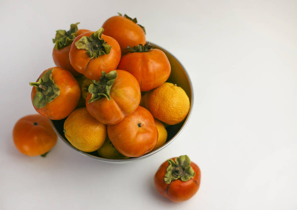 Persimmon close-up liggend in een kom op een witte achtergrond. Biologische landbouw, gezonde voeding concept, milieuvriendelijke producten, vegetarische, rauwe producten. - Foto, afbeelding