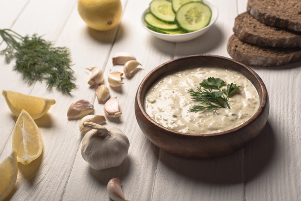 Tzatziki sauce in wooden bowl with ingredients on white wooden background - Photo, Image
