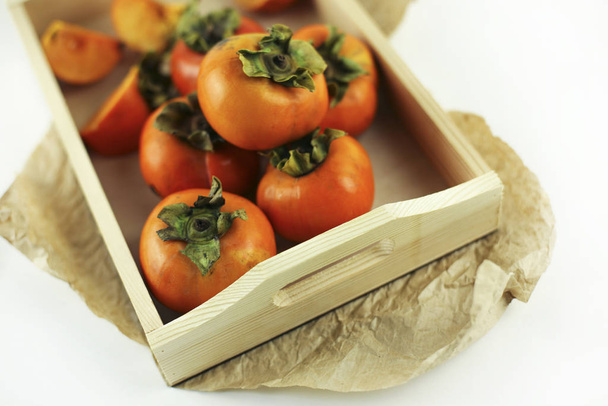 Persimmons close-up liggend in een houten kist op een witte achtergrond. Biologische landbouw, gezonde voeding concept, milieuvriendelijke producten, vegetarische, rauwe producten. - Foto, afbeelding