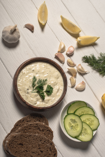 Top view of homemade tzatziki sauce with bread and ingredients on white wooden background - Photo, Image