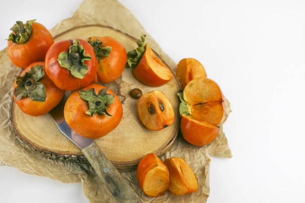 Persimmon lies on a wooden Board on a white background. Persimmon close - up whole and cut into slices with a knife. Organic farming, healthy food concept, eco-friendly products, vegetarian, raw  - Фото, изображение