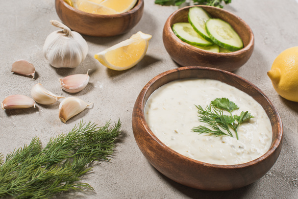 Homemade tzatziki sauce in wooden bowl with ingredients and greenery on stone background - Zdjęcie, obraz