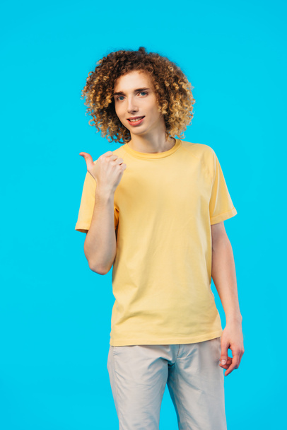 smiling curly teenager showing thumb up isolated on blue - Φωτογραφία, εικόνα
