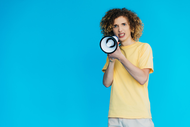 angry curly teenager screaming in loudspeaker isolated on blue - Photo, Image