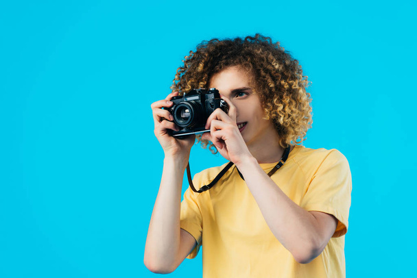 curly teenager taking picture on film camera isolated on blue - Foto, Imagem