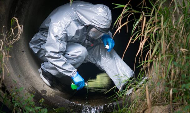 close-up, the terrorist in a protective suit and gloves, pours liquid with poison, for infection, in a drainpipe - Foto, Bild