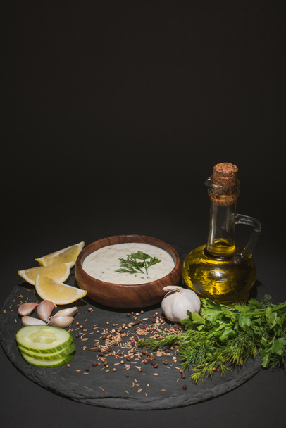 Tzatziki-Sauce mit Bio-Zutaten, Gewürzen und Olivenöl auf dunklem Brett auf schwarzem Hintergrund - Foto, Bild