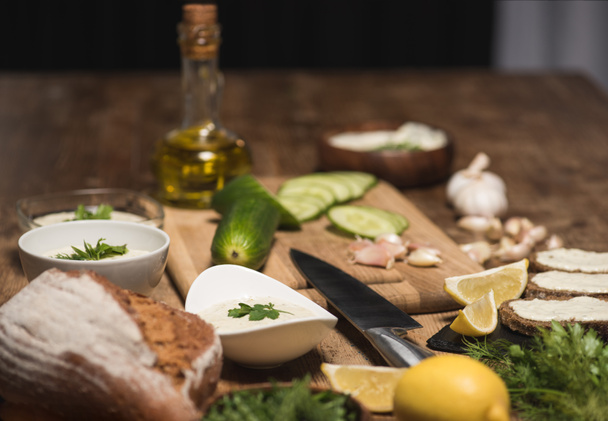 Tzatziki-Sauce mit Brot und rohem Gemüse auf dem Küchentisch  - Foto, Bild