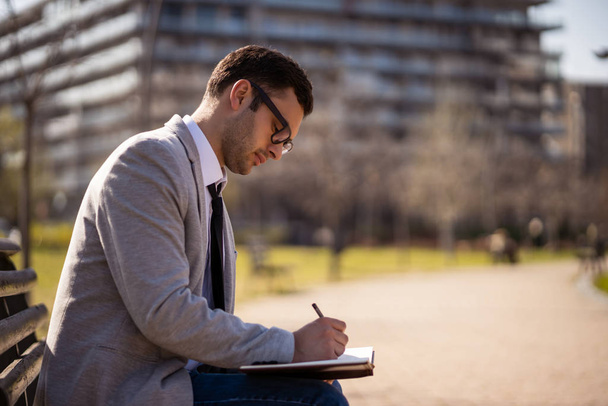 Young businessman is sitting in park and making plans. - Foto, imagen