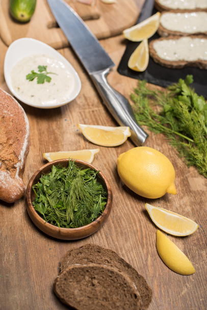 Bread, greenery and ingredients tor tzatziki sauce on wooden table  - Photo, Image