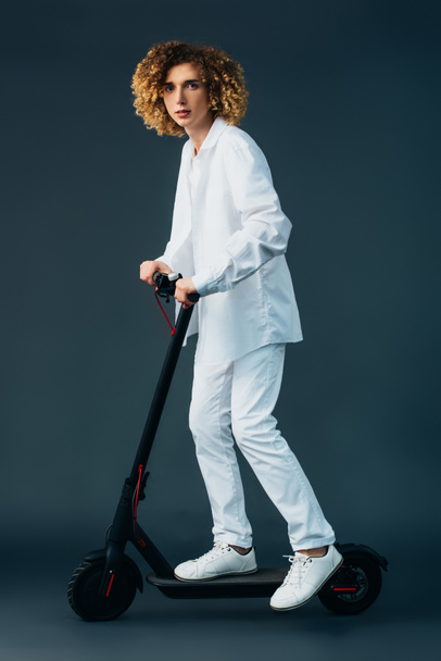 adolescent bouclé élégant en tenue blanche totale équitation scooter électrique sur vert
 - Photo, image