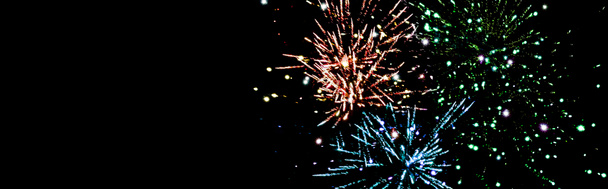 panoramic shot of blue, green and orange festive fireworks in dark night sky, isolated on black - Photo, Image