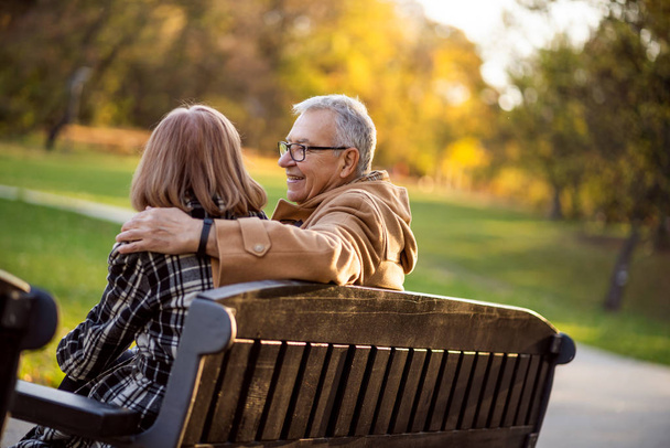 Romantisch senior koppel zit op een bankje in het park en geniet van de herfst. - Foto, afbeelding