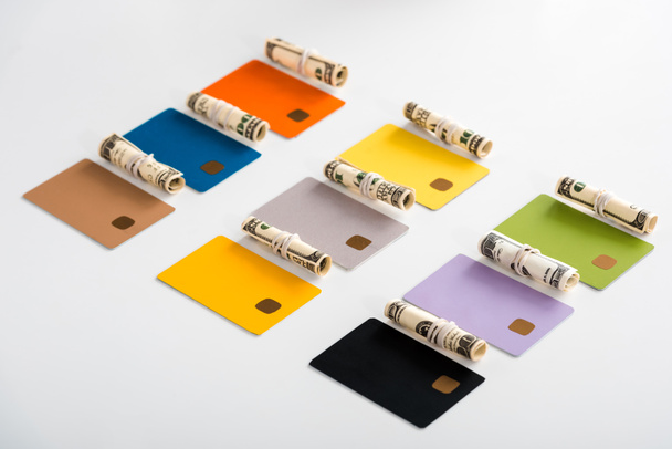 színes hitelkártya sablonok készpénz-tekercsek közelében, fehér alapon izolált dollárbankjegyekkel  - Fotó, kép