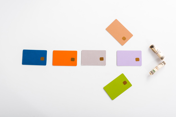 vista superior de modelos de cartão de crédito coloridos e rolos de dinheiro no branco
  - Foto, Imagem