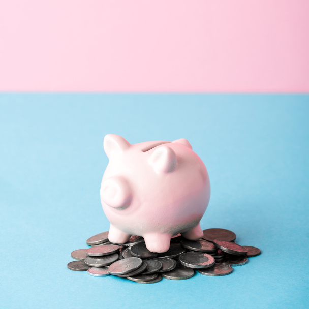 close up of coins near piggy bank isolated on blue and pink  - Foto, afbeelding