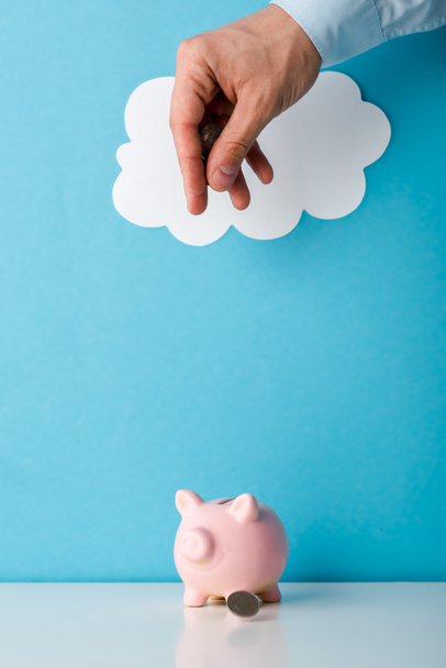cropped view of man throwing coin near pink piggy bank on blue  - Foto, Imagen