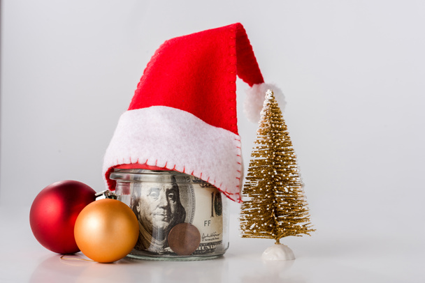 kleiner Weihnachtsbaum in der Nähe von Weihnachtskugeln und Dollarnoten auf weiß  - Foto, Bild