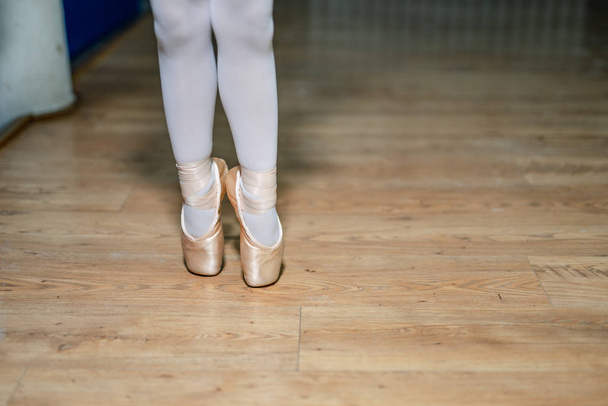 Legs of a little ballerina in a gold ballet shoes and white socks posing tiptoe in ballet hall on the floor. Closeup. - Φωτογραφία, εικόνα