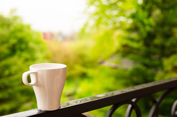 White coffee cup on the balcony with blurred nature view and forest background, after rain - Foto, imagen