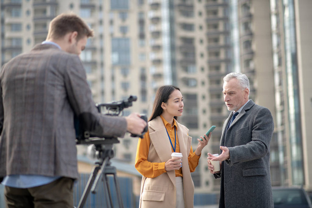 Female reporter in beige outfit asking questions to a grey-haired man - Fotó, kép