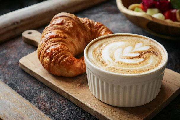 A cup of coffee with latte art on top, butter  croissant and granola with fresh tropical fruits and yogurt on table in caffee. Concept of healthy breakfast - Foto, afbeelding