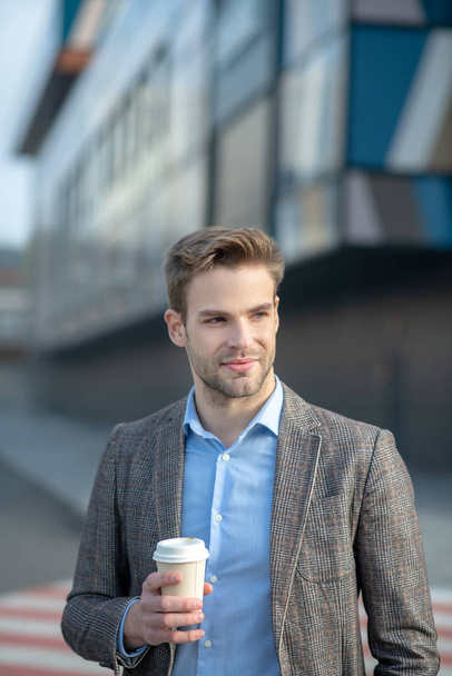 Young handsome man in a jacket holding a cup of coffee - Φωτογραφία, εικόνα