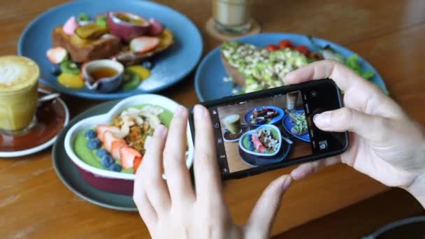 朝食のトレンド。女性ブロガーカフェで携帯電話で食べ物の写真を撮る - 映像、動画