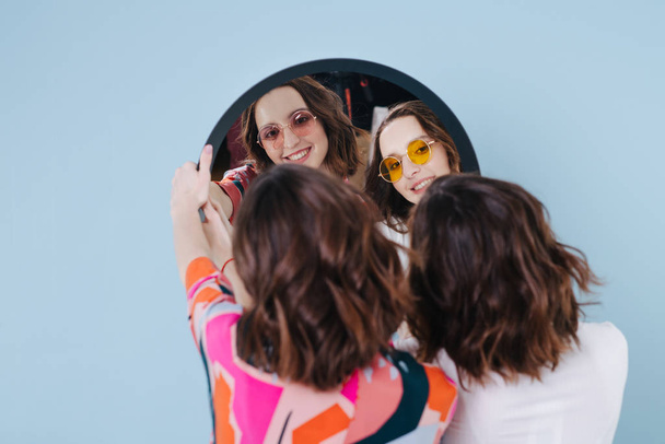 Δίδυμες αδελφές κρατούν έναν καθρέφτη και βλέπουμε την αντανάκλασή τους - Φωτογραφία, εικόνα
