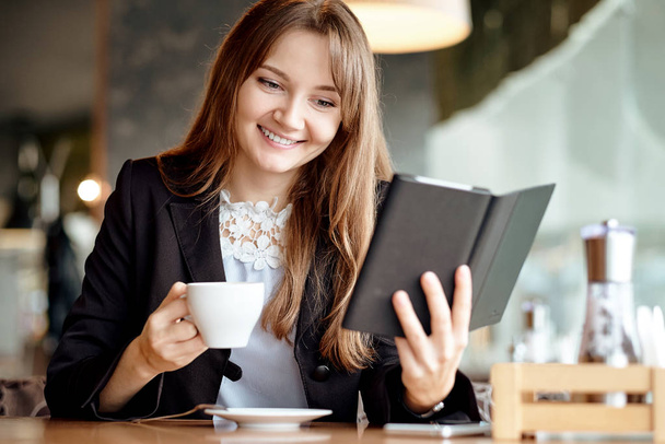 Nuori liikenainen kahvilassa lukemassa ebookia ja juomassa kahvia - Valokuva, kuva