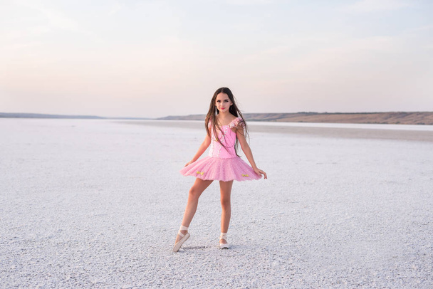 girl ballerina dancer in a pink dress on a snow-white salty dried lake. Fantastic landscape and a girl in red punata and a pink dress. - Фото, зображення