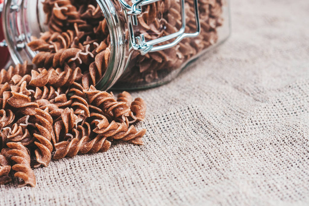 fusilli pasta - raw whole-grain Italian pasta of dark color on a linen cloth in the kitchen - copy space - Zdjęcie, obraz