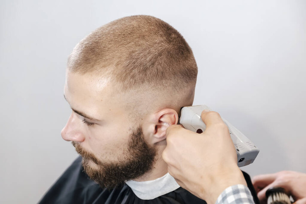 Friseur rasiert den bärtigen Kunden mit elektrischem Trimmer den Kopf - Foto, Bild
