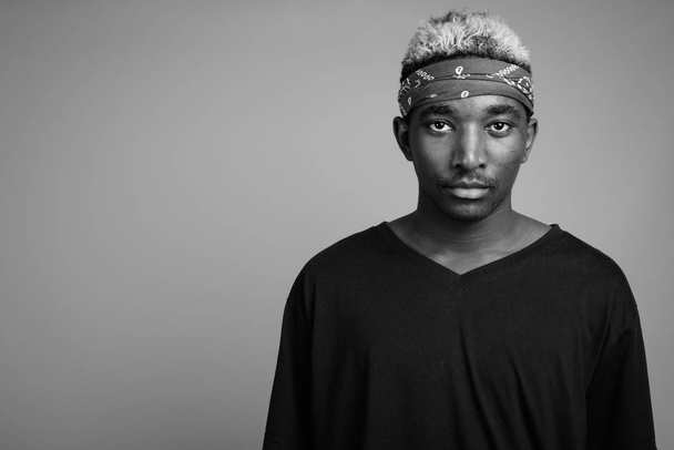 Young African man wearing bandanna as headband against gray background - Foto, Imagem