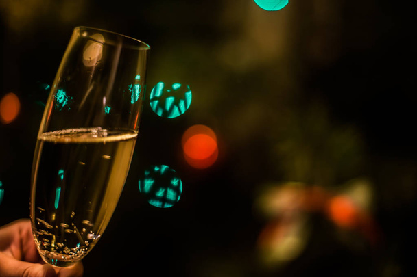 Copo com champanhe na mão em um fundo de árvore de Natal
 - Foto, Imagem